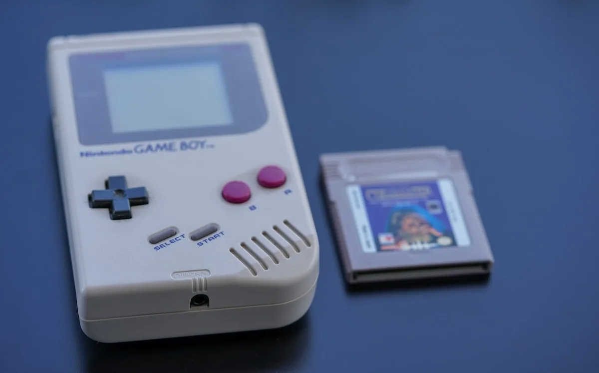 Console Game Boy branco original ao lado de um cartucho de jogo sobre superfície azul escura