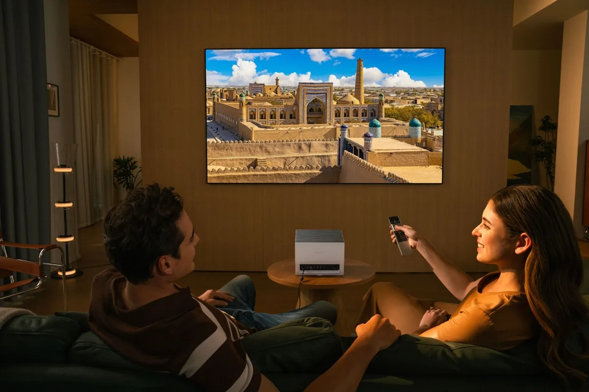 Projetor gamer em uso numa sala de estar Casal assistindo em sofá a uma imagem grande projetada na parede da sala, com projetor sobre mesa entre os dois