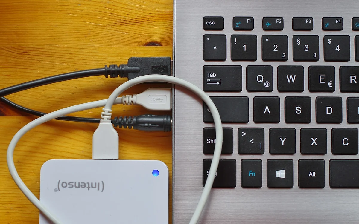 Mão segurando um SSD externo portátil ao lado de um notebook aberto