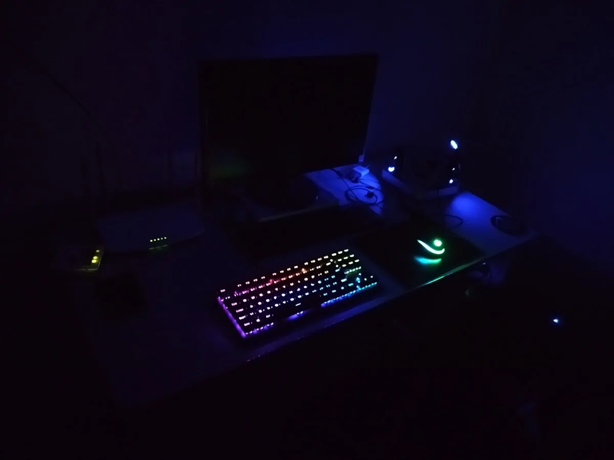 Teclado e mouse RGB sincronizados por software Teclado mecânico com iluminação RGB multicolorida aceso sobre mesa escura, mouse com logo verde ao lado