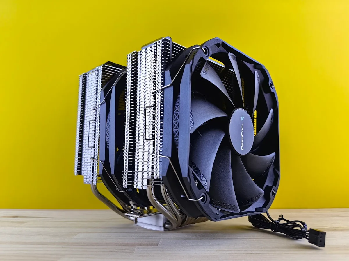 Cooler de CPU dual-tower Deepcool na cor preta com heat pipes expostos e ventoinha central, sobre fundo amarelo