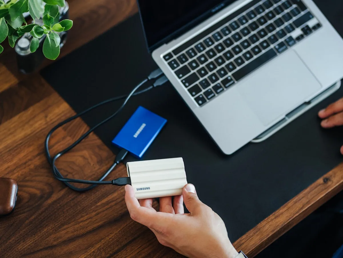 Notebook com dois cabos USB-C conectados diretamente a SSDs externos sobre mesa de madeira
