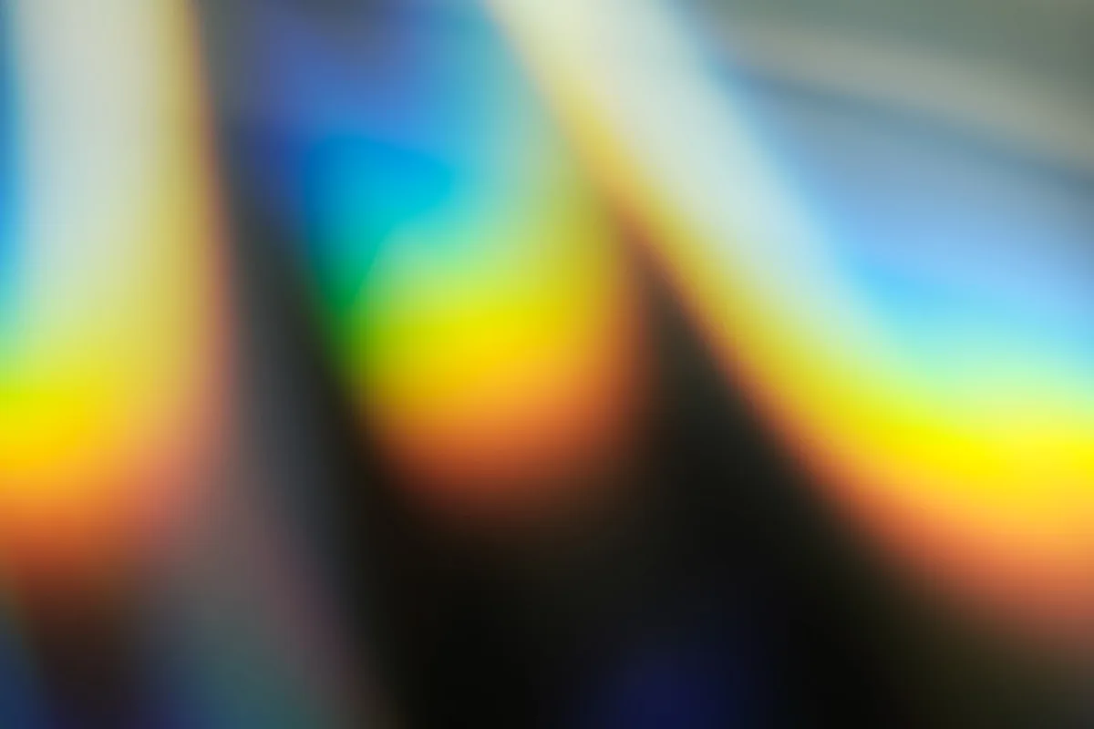 Separação de cores em feixe de luz Reflexos de luz coloridos em diagonal formando faixas de azul, amarelo e vermelho sobre fundo escuro
