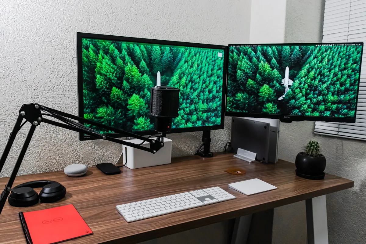 Dois monitores em braços articulados com microfone de mesa entre as telas em home office claro