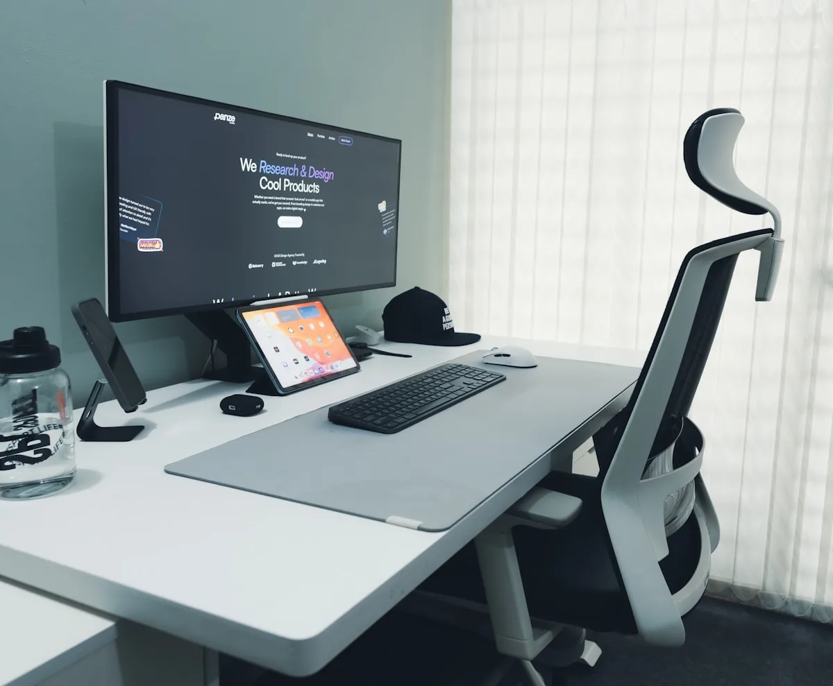 Monitor sobre suporte de mesa articulado ao lado de cadeira ergonômica clara em home office