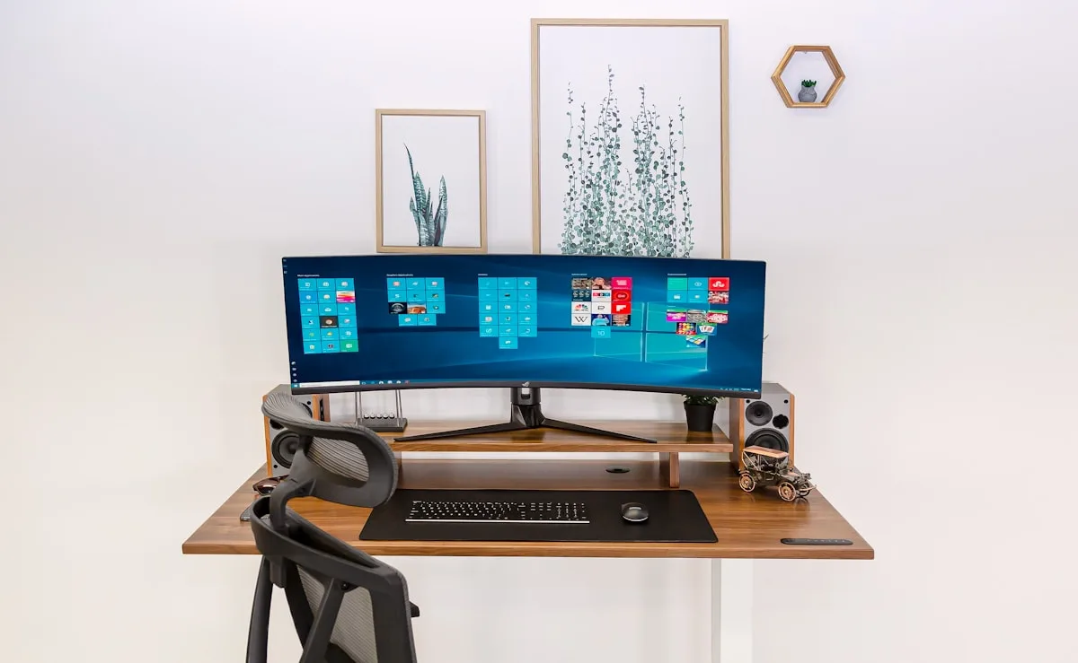 Setup de home office com monitor elevado por suporte articulado Monitor ultrawide curvo elevado sobre suporte de mesa em home office claro e organizado