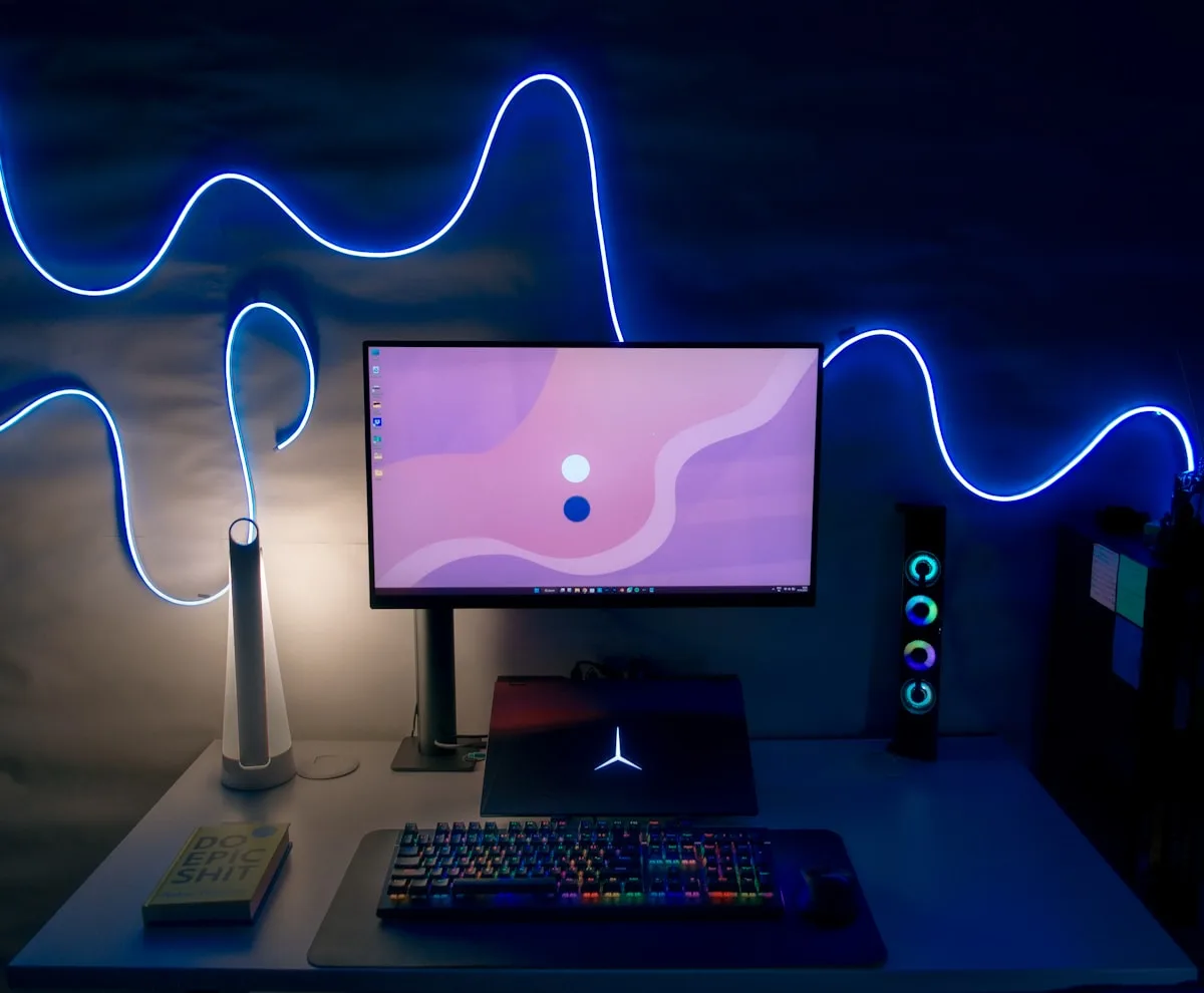 Fita LED RGB decorando o setup gamer Fita de LED formando desenho ondulado azul neon na parede atrás do monitor em quarto escuro