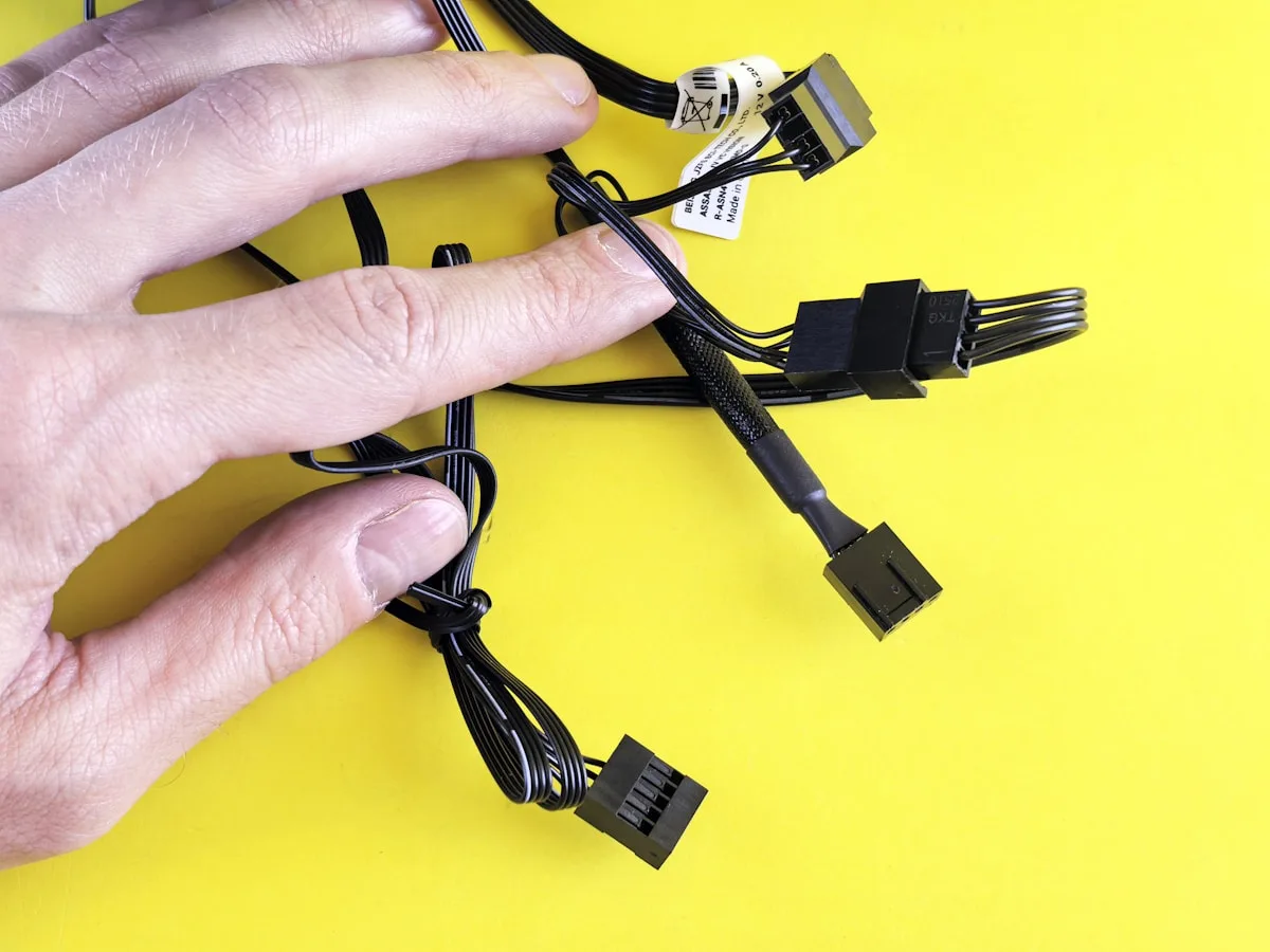 Mão segurando um conjunto de cabos modulares desconectados de uma fonte de PC sobre fundo amarelo