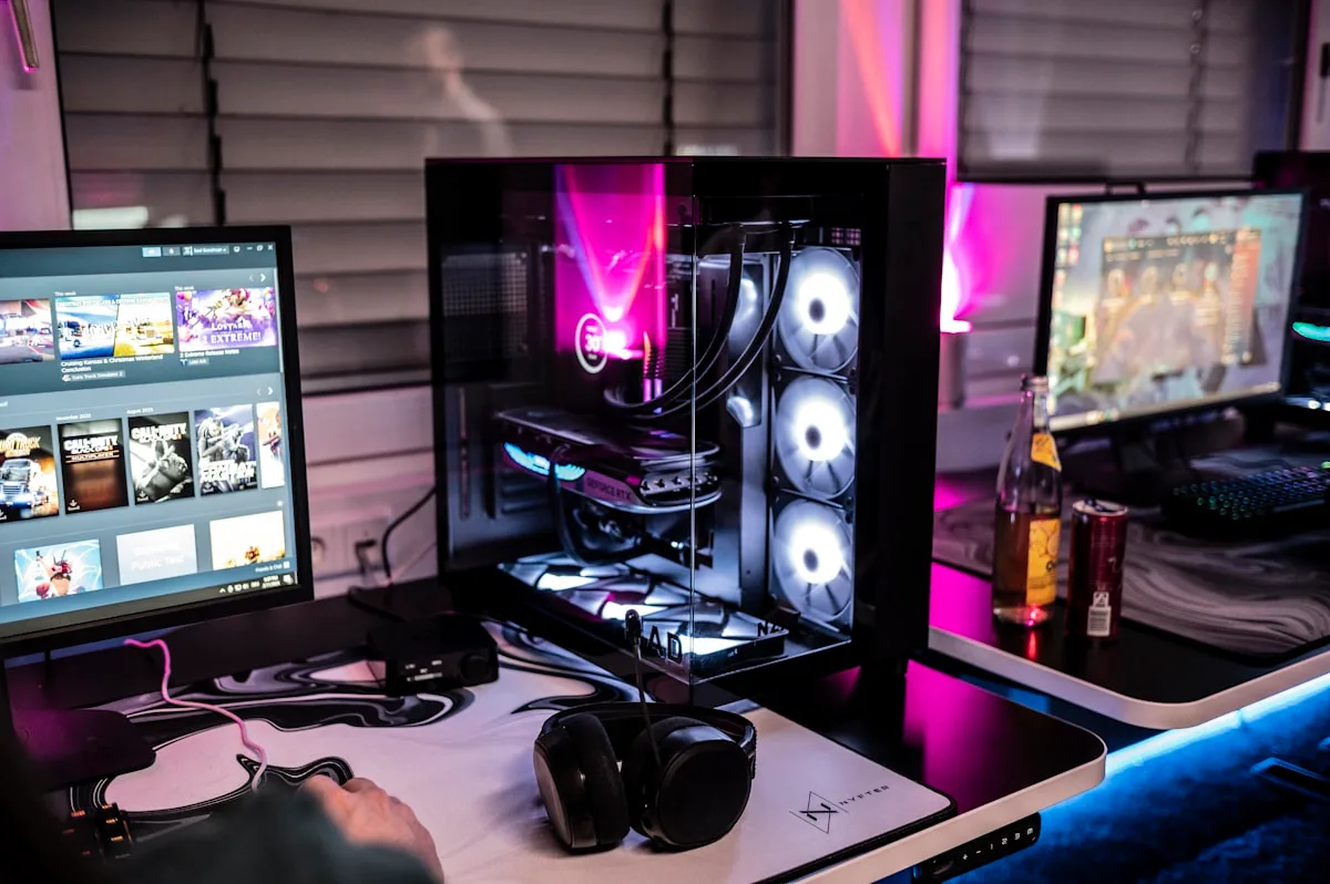 Setup gamer com gabinete de vidro lateral iluminado, três ventoinhas brancas visíveis e dois monitores sobre a mesa