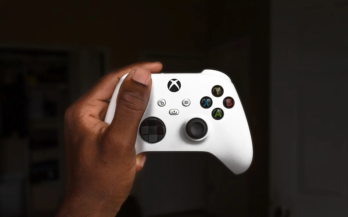 Controle sem fio do Xbox Mão segurando o controle sem fio branco do Xbox em ambiente com pouca luz