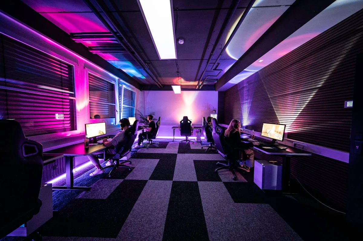 Sala de jogos com iluminação ambiente rosa e roxa refletindo nas paredes ao redor das mesas