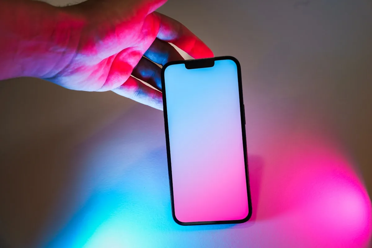 Controle de cena de luz pelo aplicativo Mão segurando smartphone com tela iluminada em rosa e azul controlando cena de luz ambiente