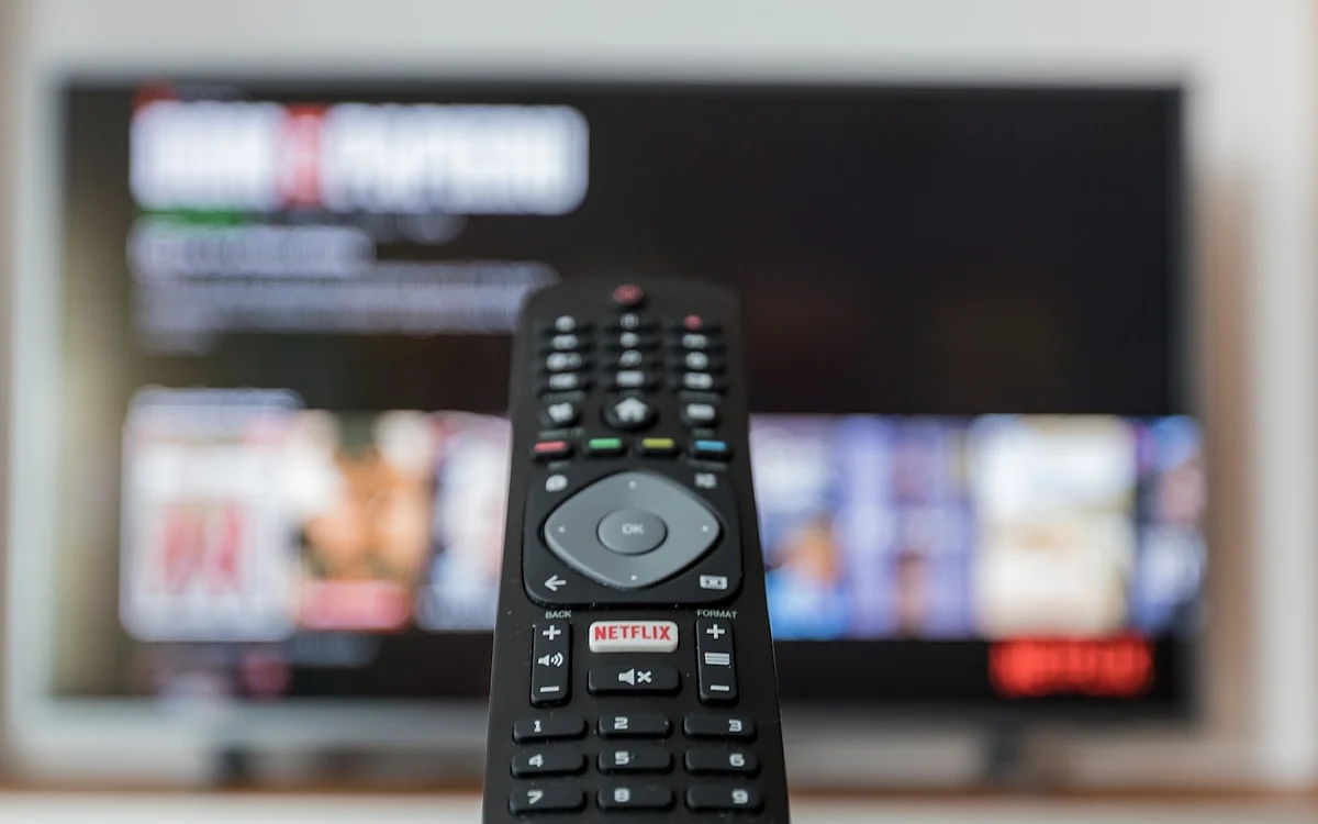 Decisão na tela de streaming Controle remoto com botão de app de streaming apontado para uma TV exibindo conteúdo desfocado