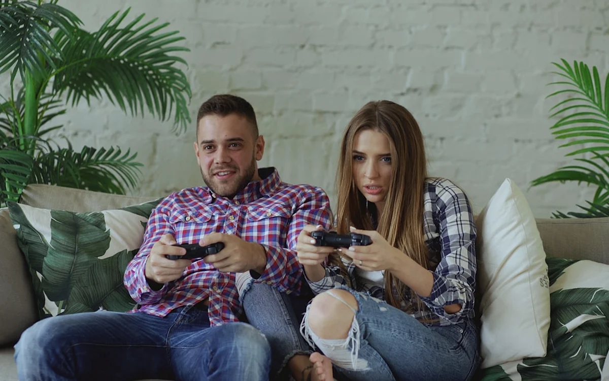 Sem data oficial para o multiplayer Casal sentado no sofá joga vídeogame junto, cada um segurando um controle nas mãos