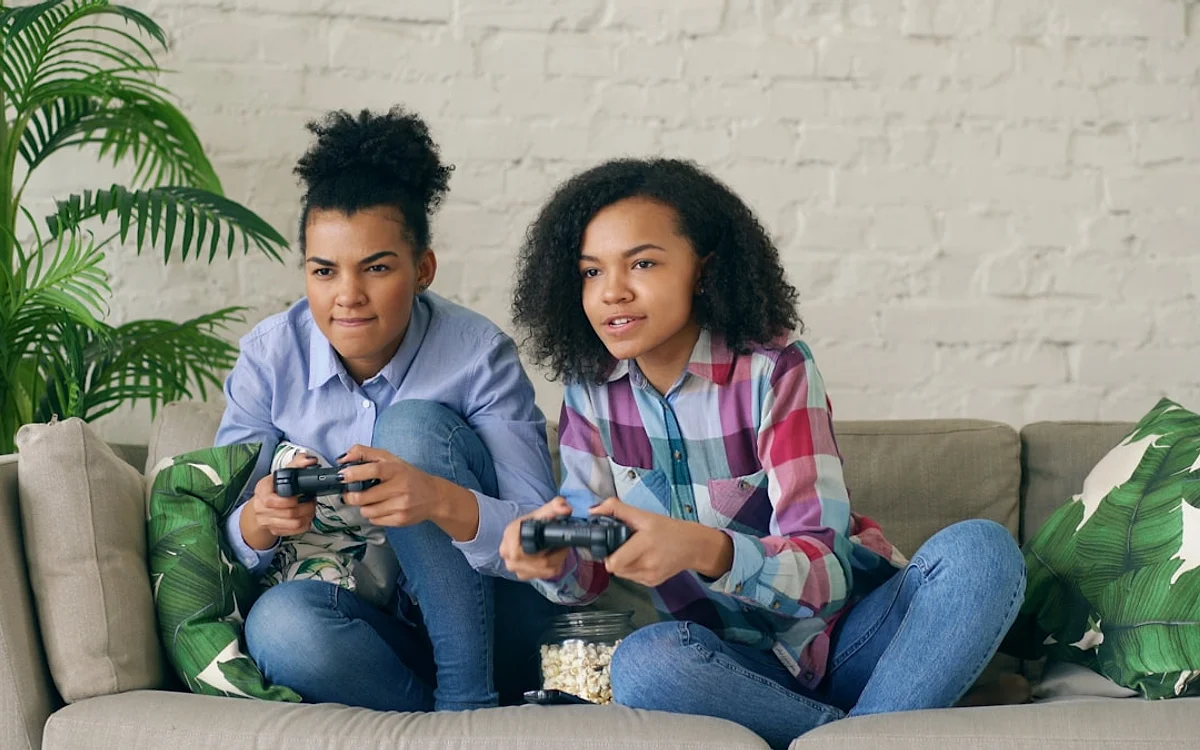 Fato ou especulação sobre o multiplayer Duas jogadoras sentadas no sofá jogam vídeogame juntas com um pote de pipoca ao lado