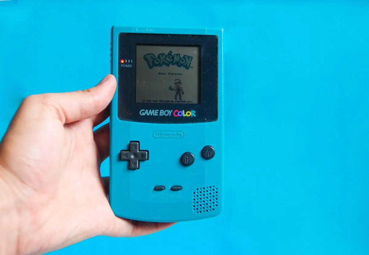 Console portátil retrô azul segurado na mão exibindo jogo clássico na tela