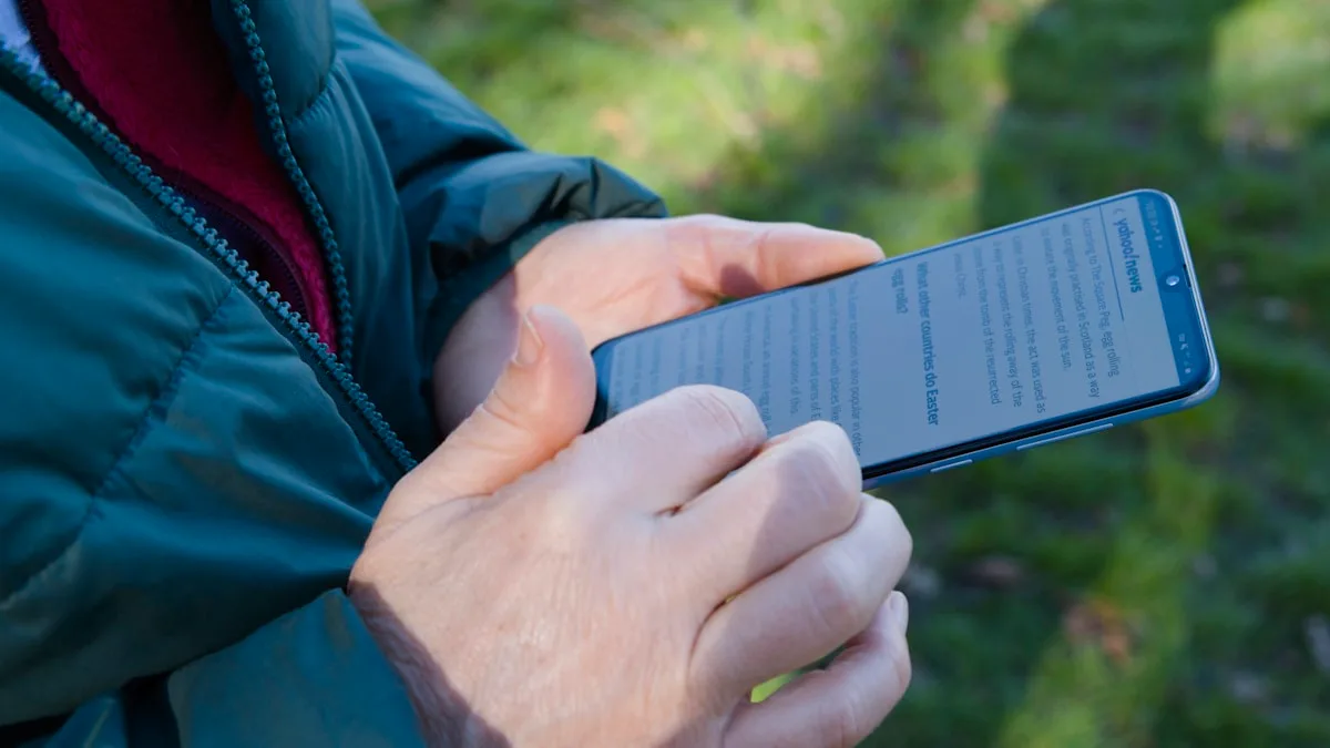Mão segurando um smartphone ao ar livre, representando o lado celular do comparativo