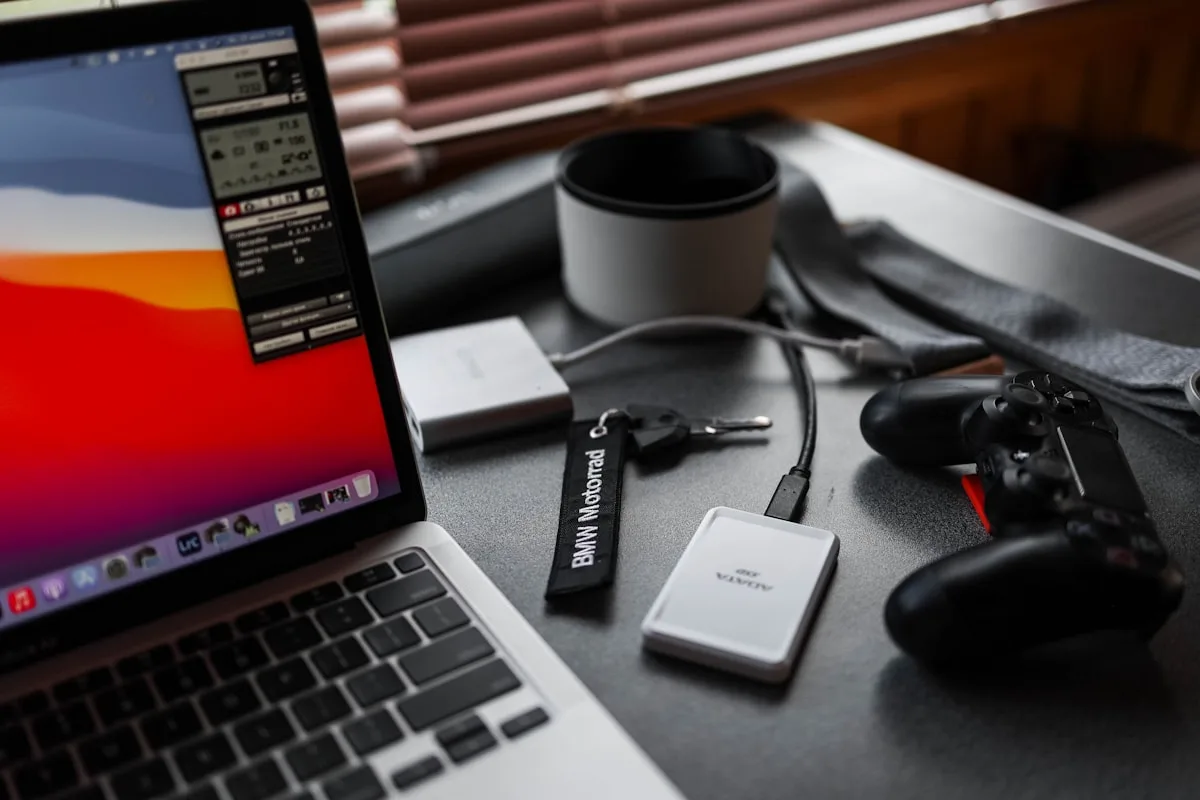 Notebook aberto sobre a mesa conectado a SSD portátil e controle de videogame por cabo USB