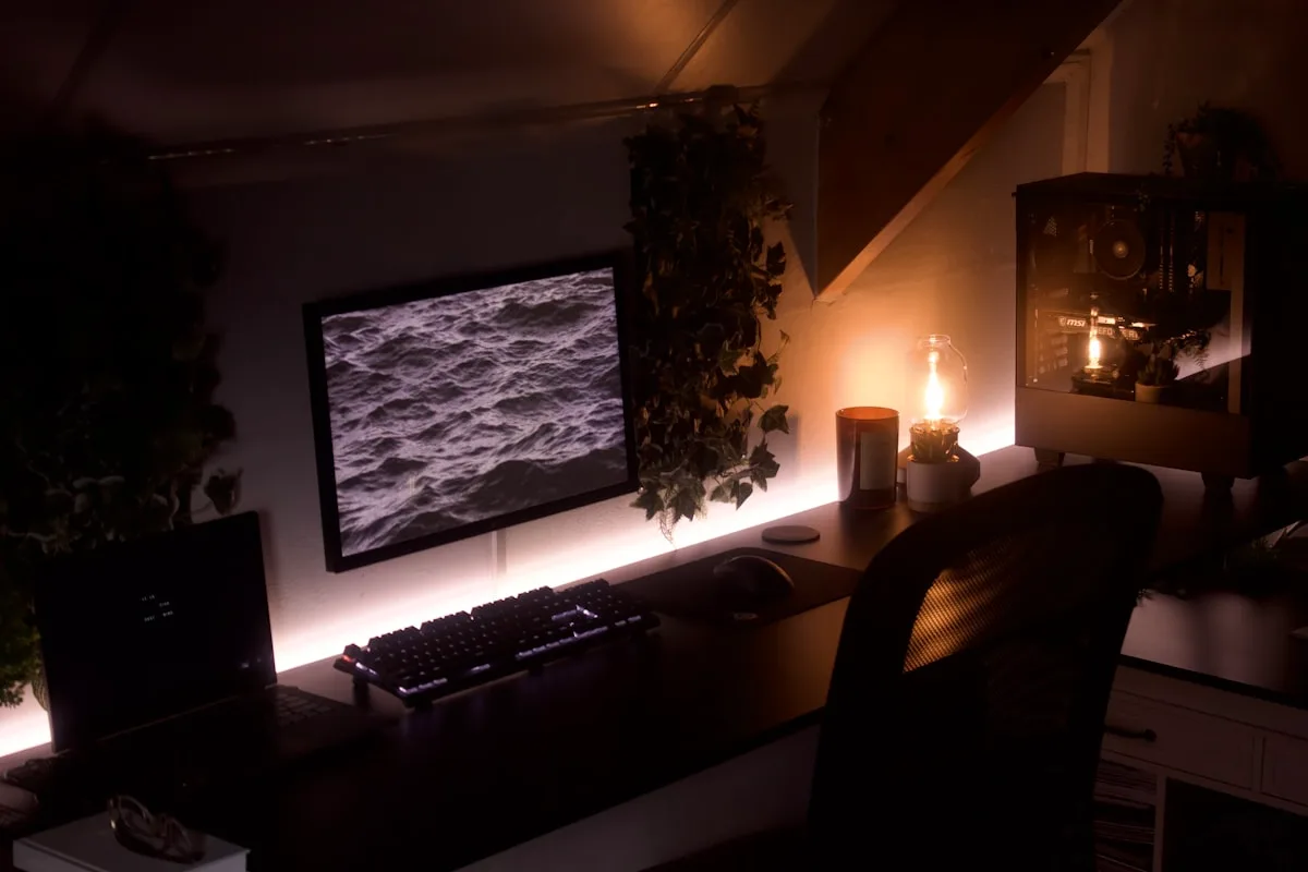 Mesa gamer com luz âmbar suave atrás do monitor e computador ao fundo