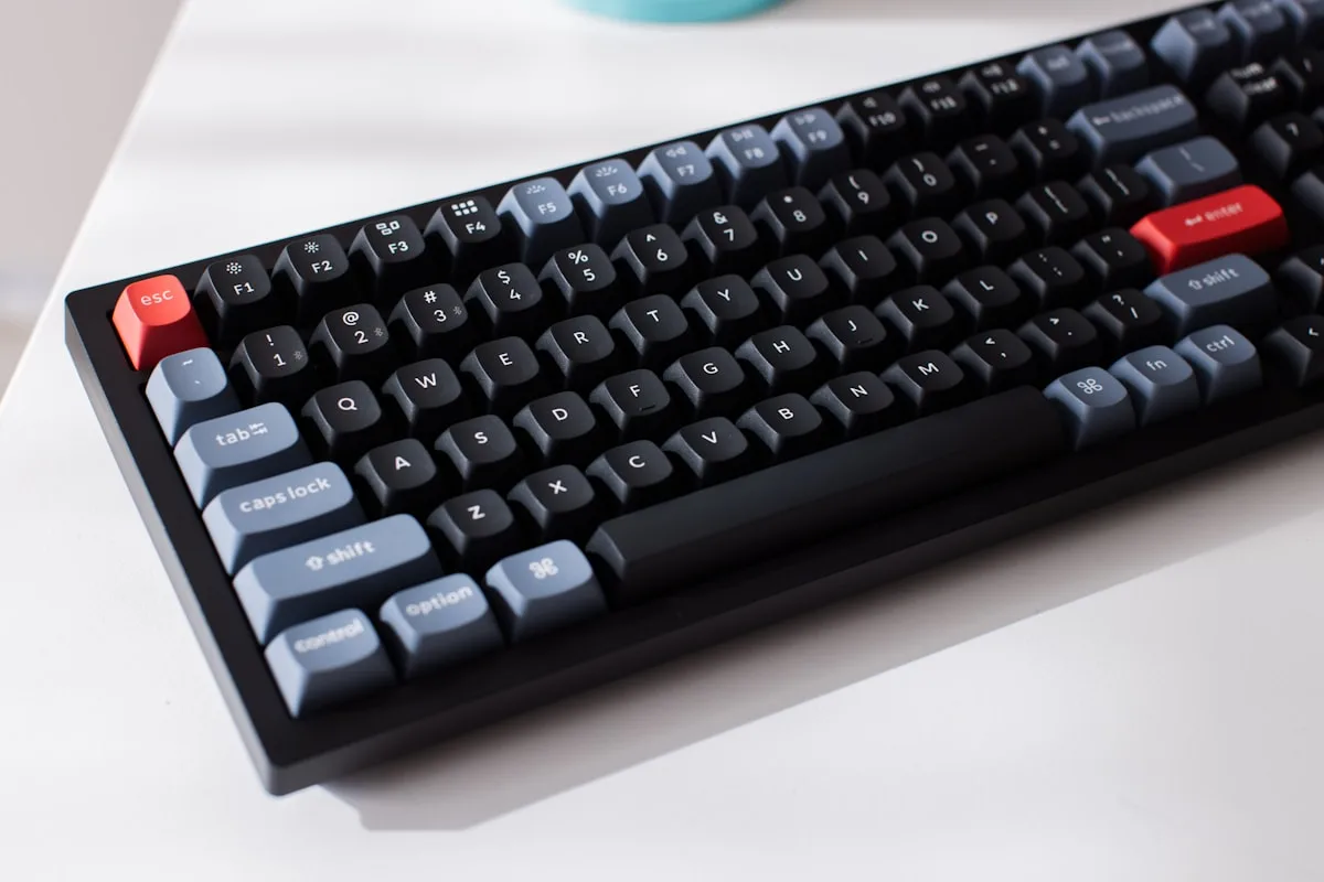Teclado mecânico TKL sem fio de corpo robusto ao lado de notebook em mesa de trabalho