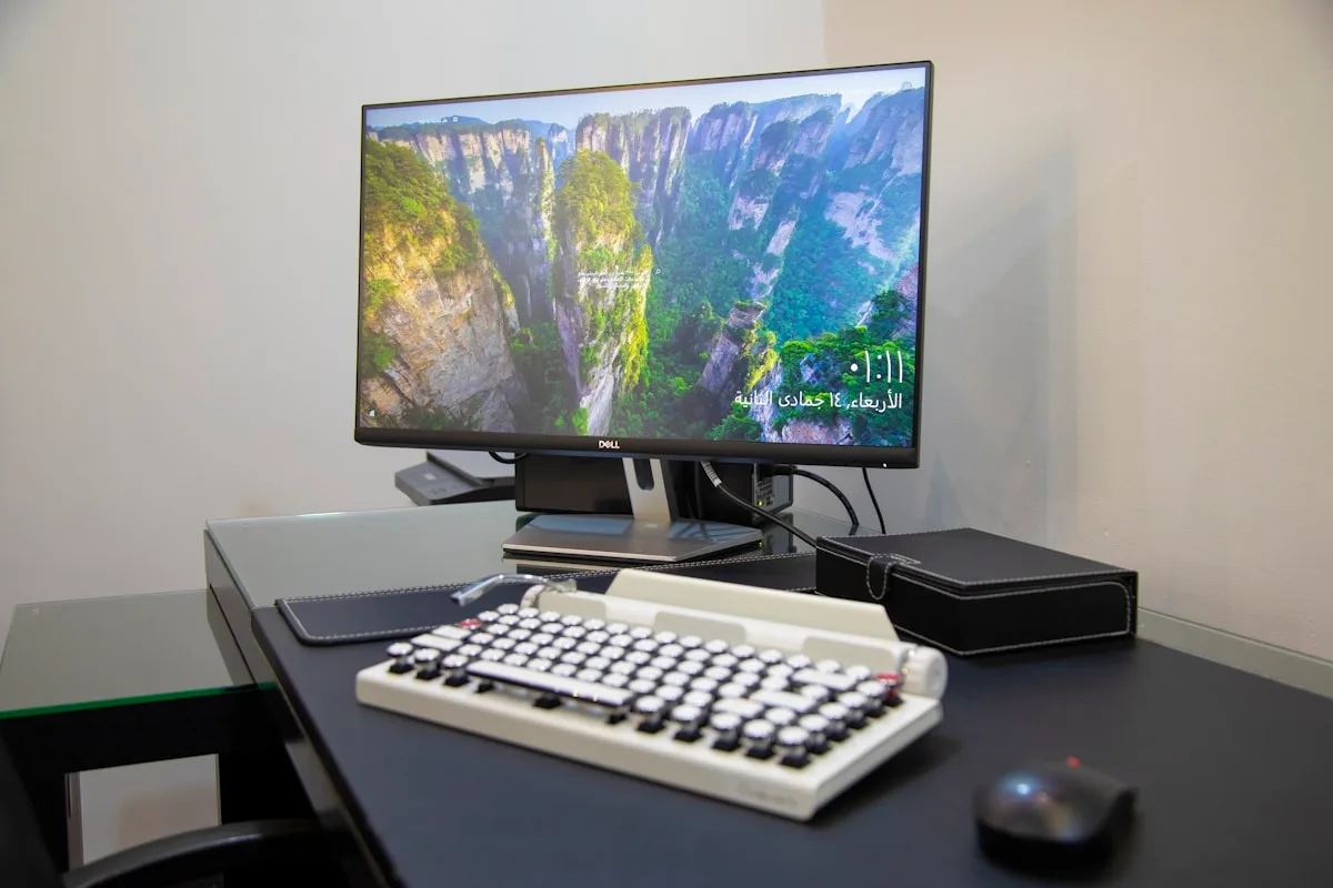 Mesa com monitor conectado a uma caixa preta de KVM switch, teclado retrô e mouse sem fio