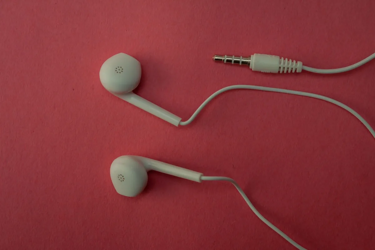 Fones intra-auriculares com fio e cabo branco sobre superfície rosa