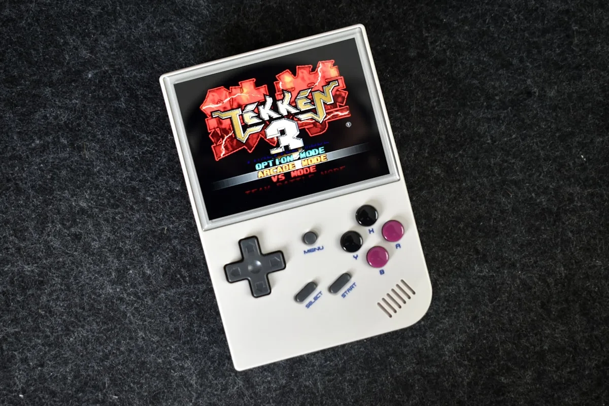 Handheld retrô genérico com D-pad exibindo jogo de PlayStation emulado na tela