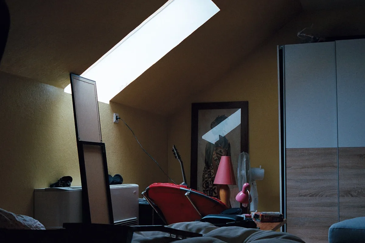 Ambiente residencial que pode receber fita LED de entrada Quarto de teto inclinado com pouca luz entrando pela claraboia e guarda-roupa ao fundo