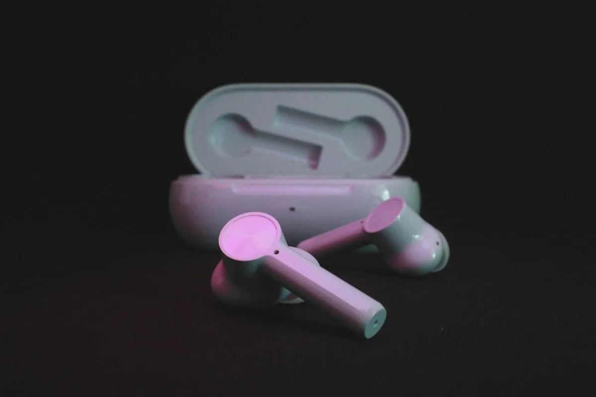 Earbuds em tons rosa e branco sobre fundo neutro para ilustrar áudio sem fio de baixa latência