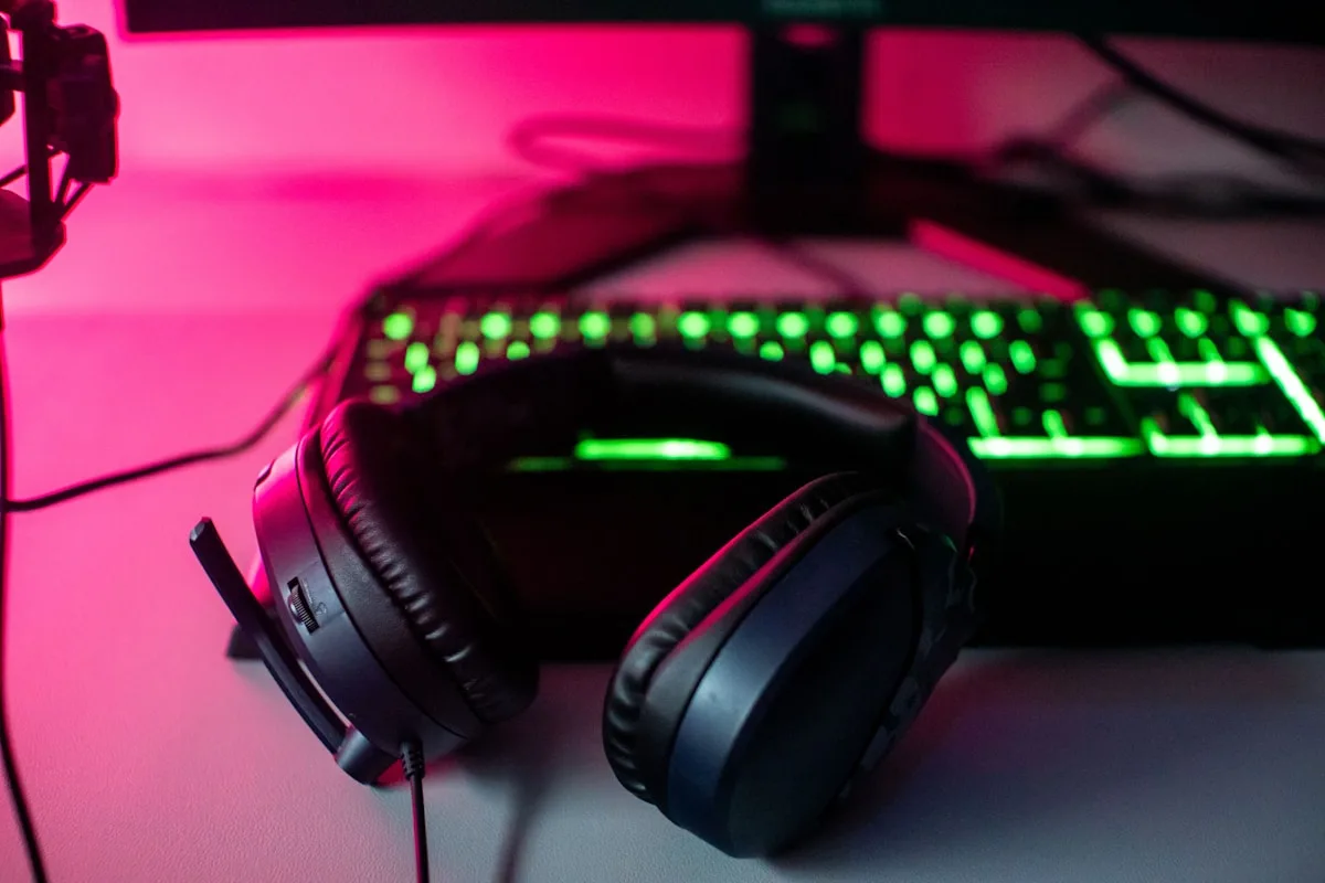 Fone in-ear sobre mesa de setup com teclado, monitor e iluminação gamer ao fundo