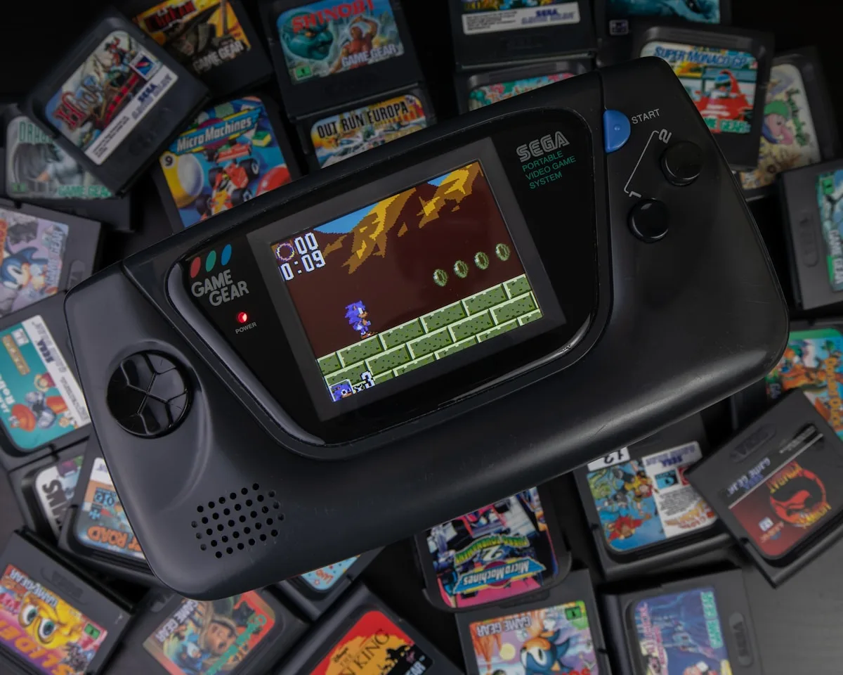 Sega Game Gear ligado sobre uma pilha de cartuchos coloridos de jogos clássicos