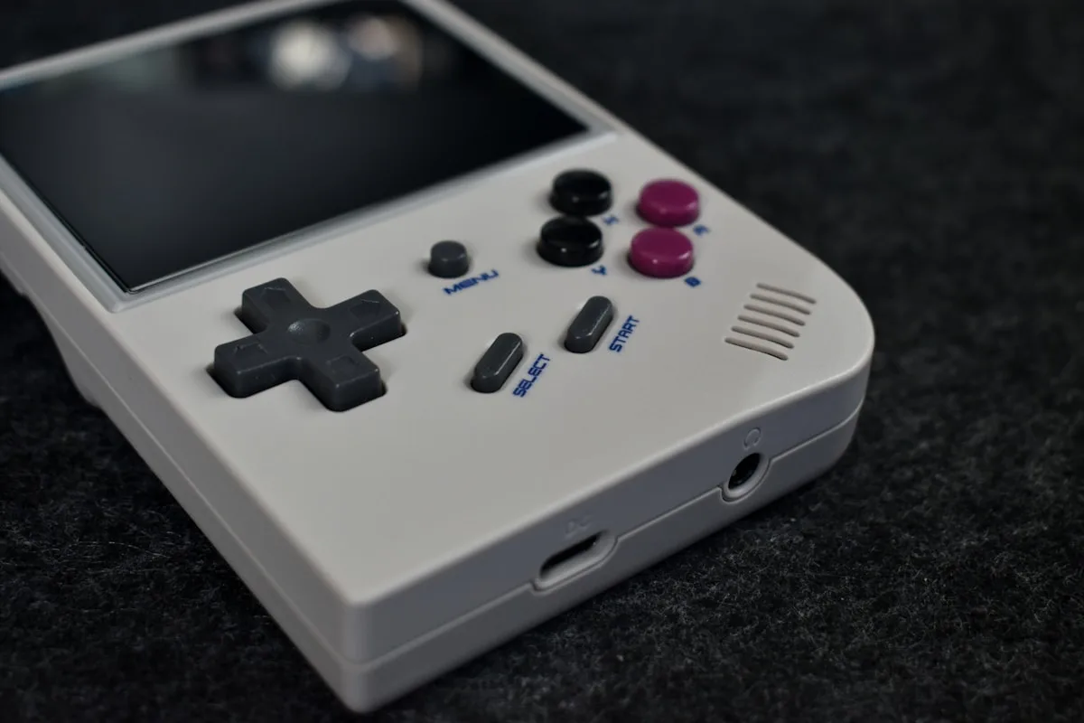 Detalhe de handheld retrô branco mostrando D-pad, botões de ação e conector de fone de ouvido