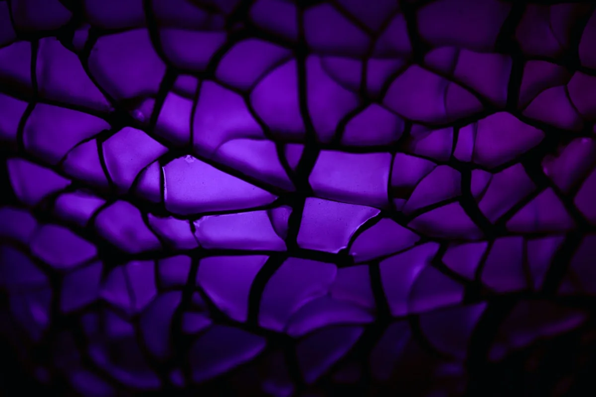 Textura em mosaico roxo escuro com rachaduras iluminadas por trás, remetendo ao preto profundo de uma tela OLED