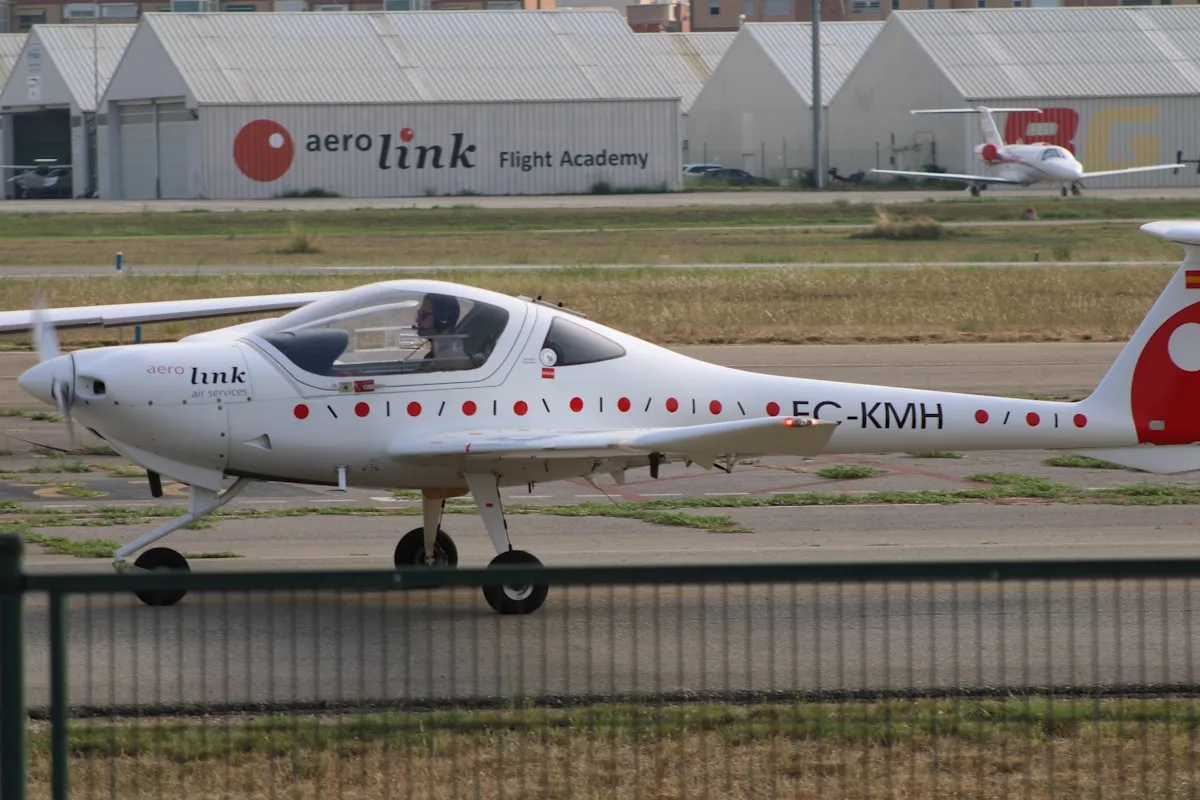 Avião monomotor de instrução estacionado na pista de um aeroclube, hangares ao fundo