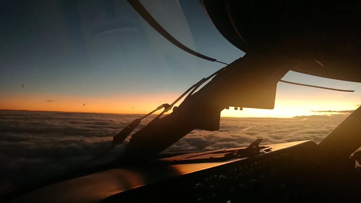 Vista do interior de um cockpit de avião ao entardecer, acima das nuvens, com a silhueta da estrutura da cabine
