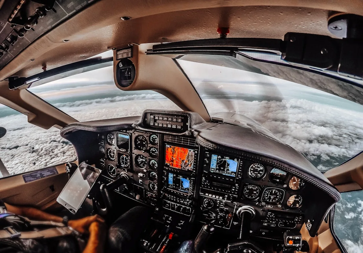 Cabine de avião pequeno sobrevoando um mar de nuvens, painel de instrumentos completo à mostra