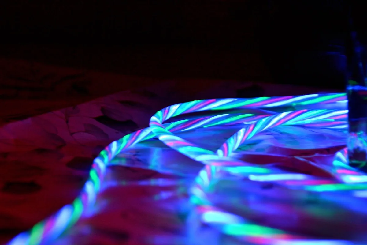 Fita de LED verde-água e rosa entrelaçada brilhando sobre superfície de mármore no escuro