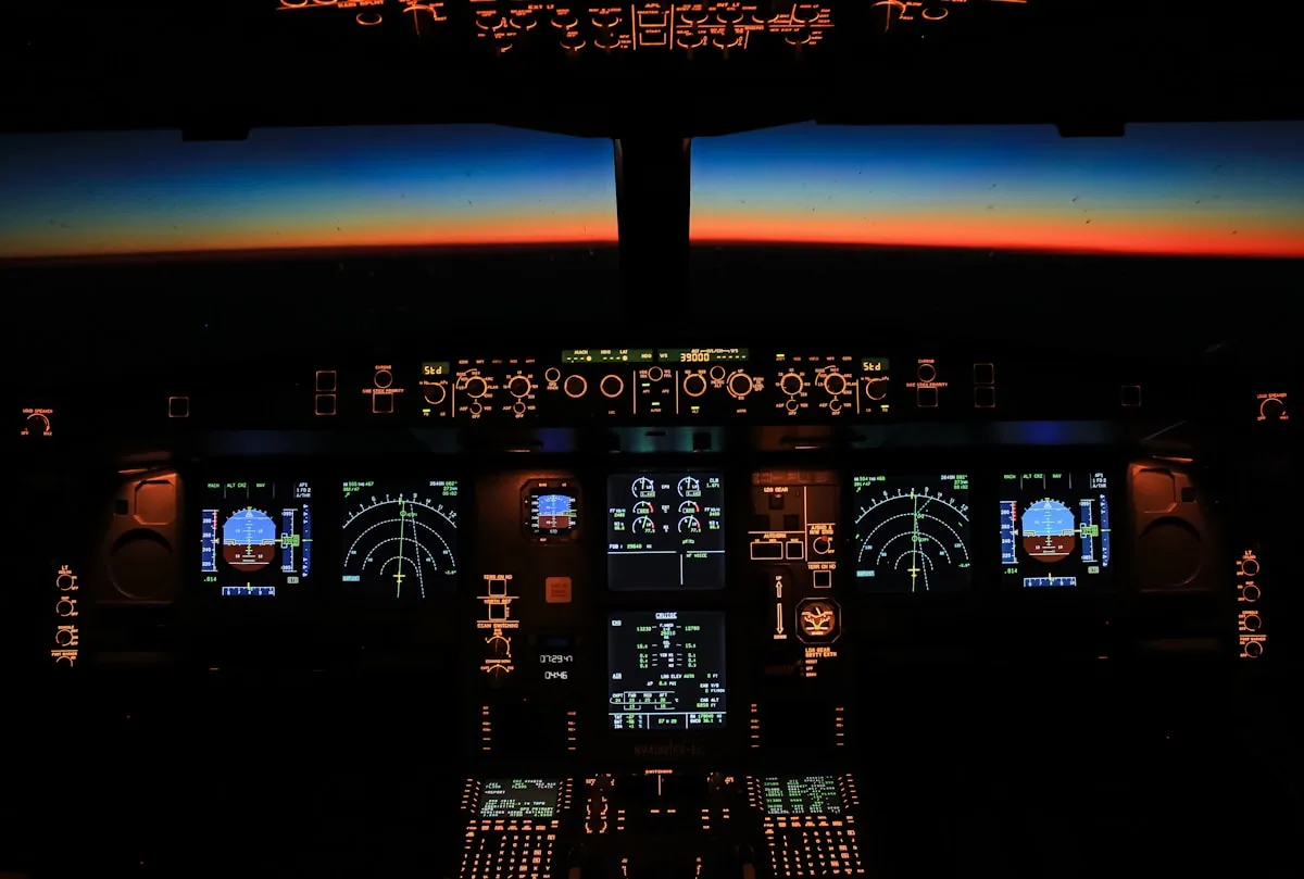 Painel de instrumentos iluminado de uma cabine de avião comercial ao entardecer, com o horizonte visível pelo para-brisa