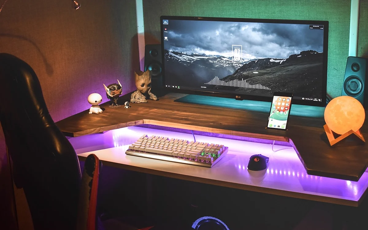 Vantagens do formato em L para setup gamer com múltiplos monitores Mesa gamer em L com monitor arm e setup organizado mostrando duas frentes de trabalho
