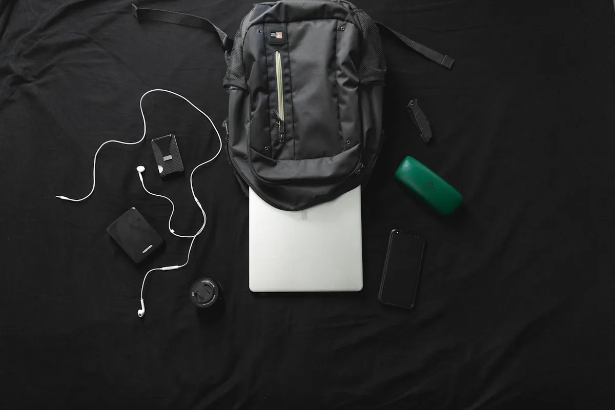 Mochila gamer preta apoiada sobre notebook fechado com fones e power bank ao redor