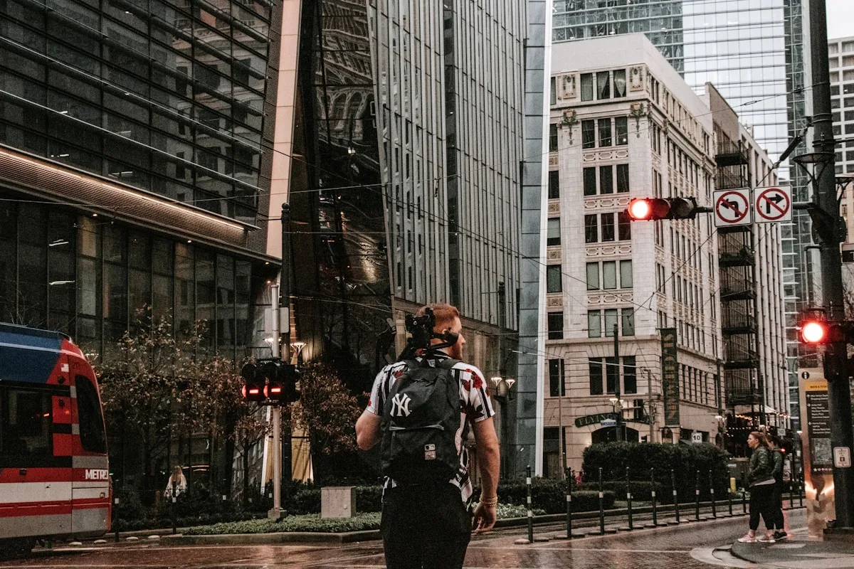 Pessoa atravessando rua movimentada na chuva com mochila nas costas em dia nublado