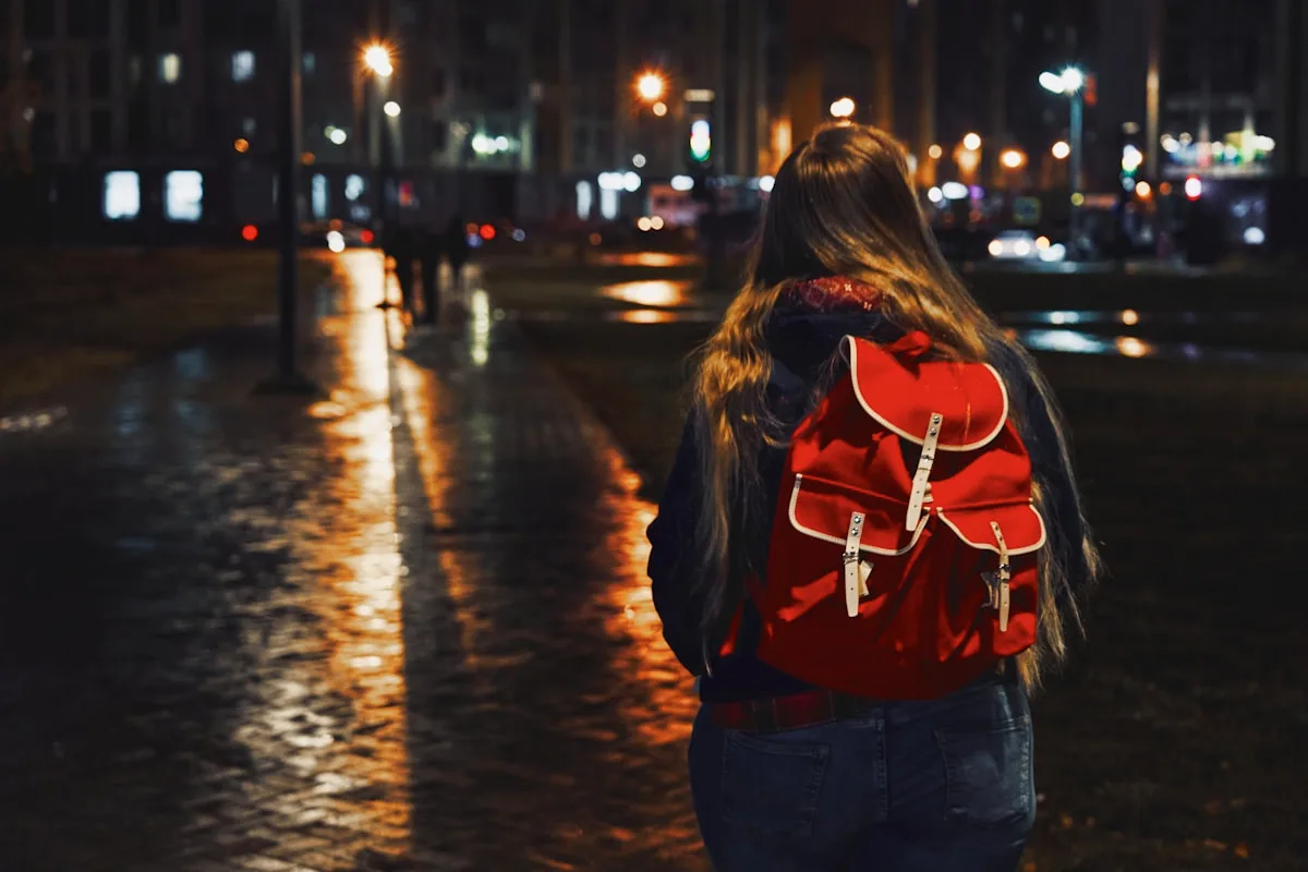 Pessoa caminhando à noite em rua molhada com mochila vermelha nas costas