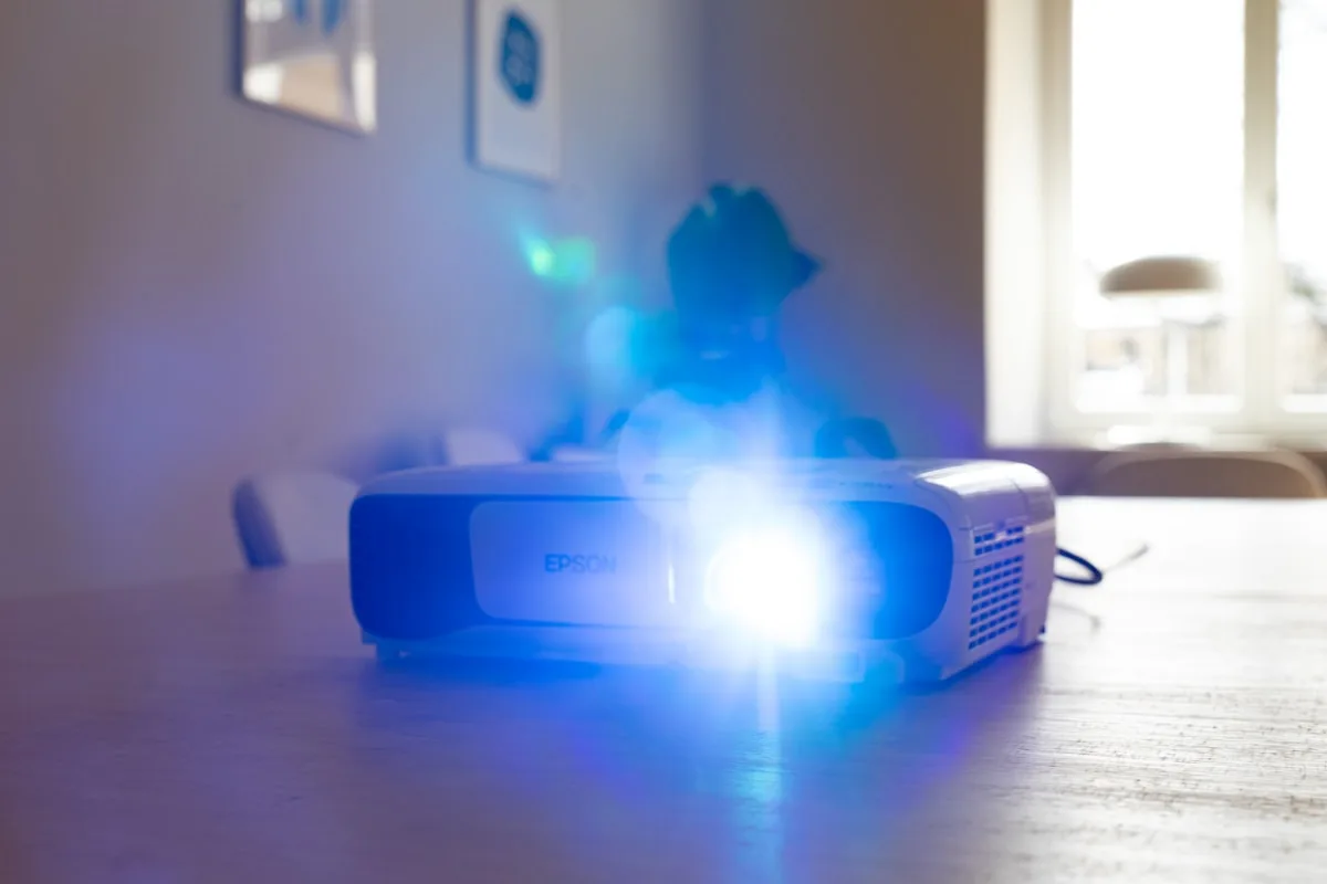 Projetor gamer até R$ 1.000 em ambiente escurecido Ambiente doméstico escurecido com feixe de luz de projetor formando retângulo de imagem na parede
