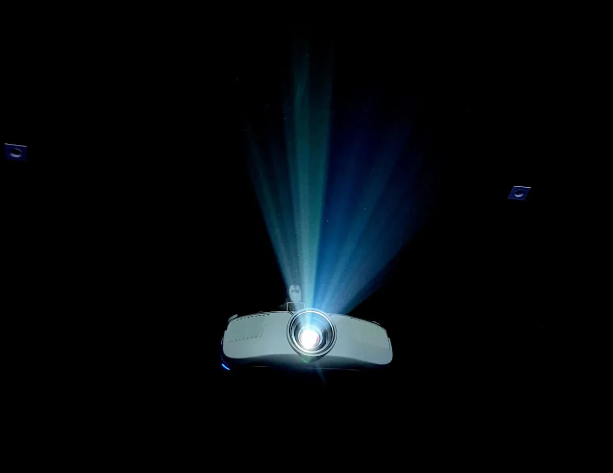 Projetor gamer até R$ 3.000 em ambiente escurecido Projetor pequeno projetando feixe de luz azulado num ambiente completamente escuro