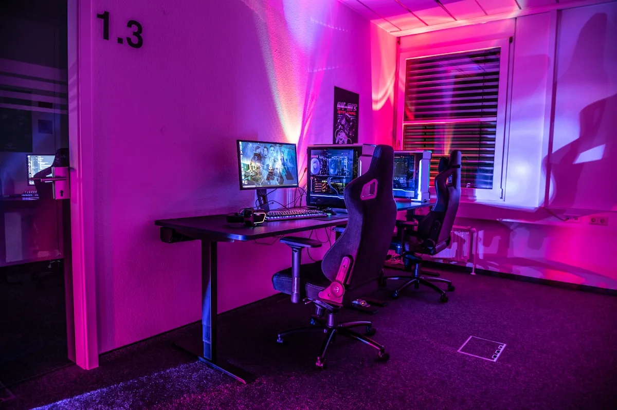 Ambiente de jogos para projetor Optoma Setup gamer com PCs, monitores e cadeiras em sala iluminada de roxo e rosa