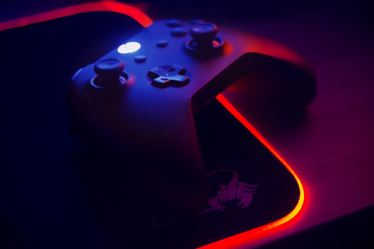 Setup escuro com Xbox Series X e projetor gamer Controle de videogame em ambiente escuro com iluminação RGB vermelha e azul sobre mousepad