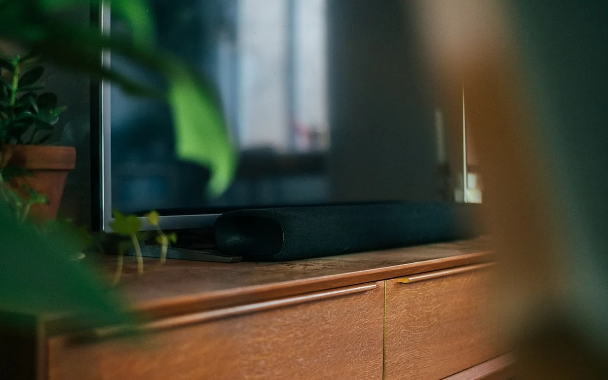 Ranking das melhores soundbars para TV em 2026 Soundbar 2.1 posicionada abaixo de TV 55 polegadas com subwoofer sem fio em sala de estar