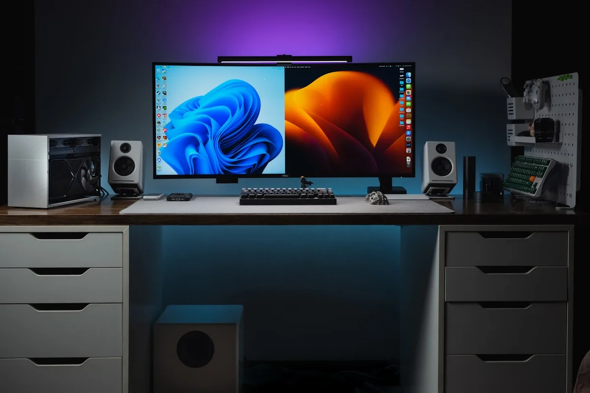 Setup com dois monitores organizados sobre a mesa Mesa com monitor curvo e monitor secundário lado a lado em setup gamer com iluminação ambiente