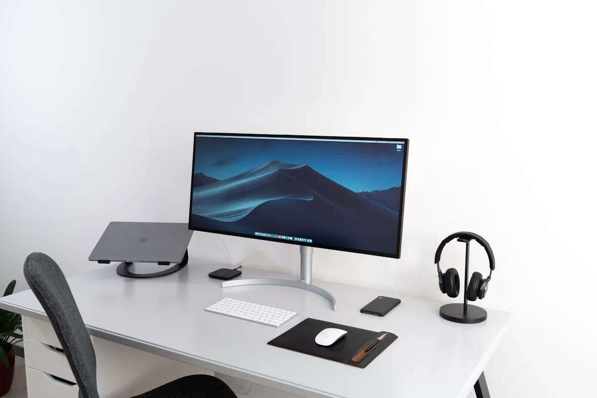 Setup organizado com monitor sobre suporte de mesa Mesa clean com monitor widescreen sobre suporte de mesa, teclado e headset ao lado