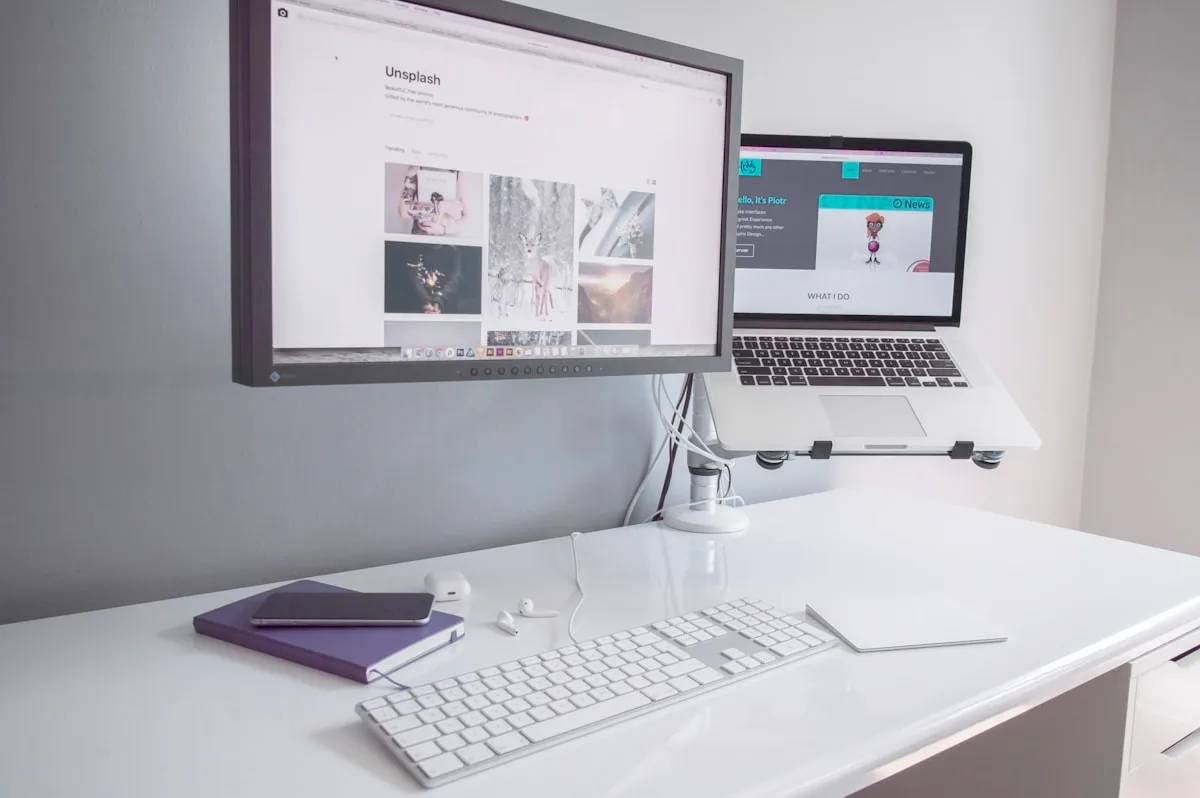Exemplo de braço articulado em uso num setup de mesa Monitor preso por braço articulado ao lado de notebook elevado em suporte também articulado